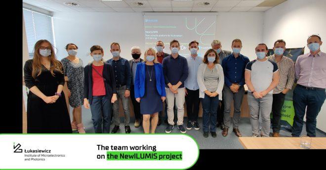 grupa ludzi w maseczkach w sali konferencyjnej. Podpis "The team working on the NewILUMIS project
